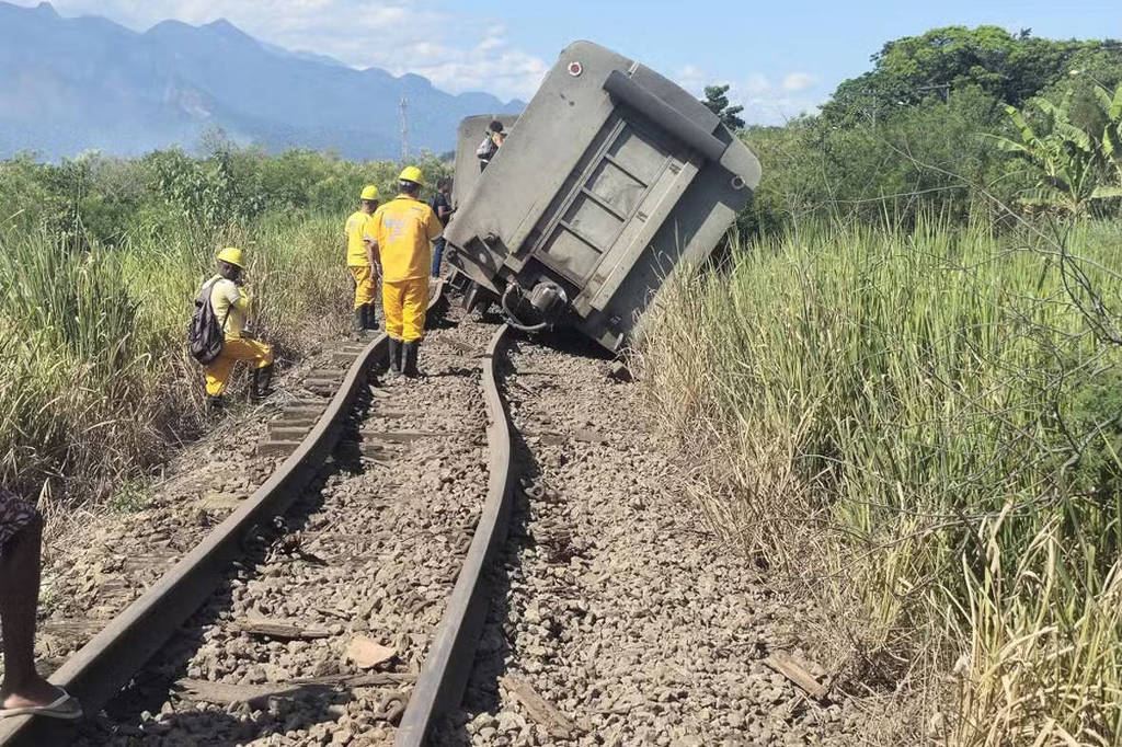 Derailed train beside buckled rails, with workers in yellow uniforms