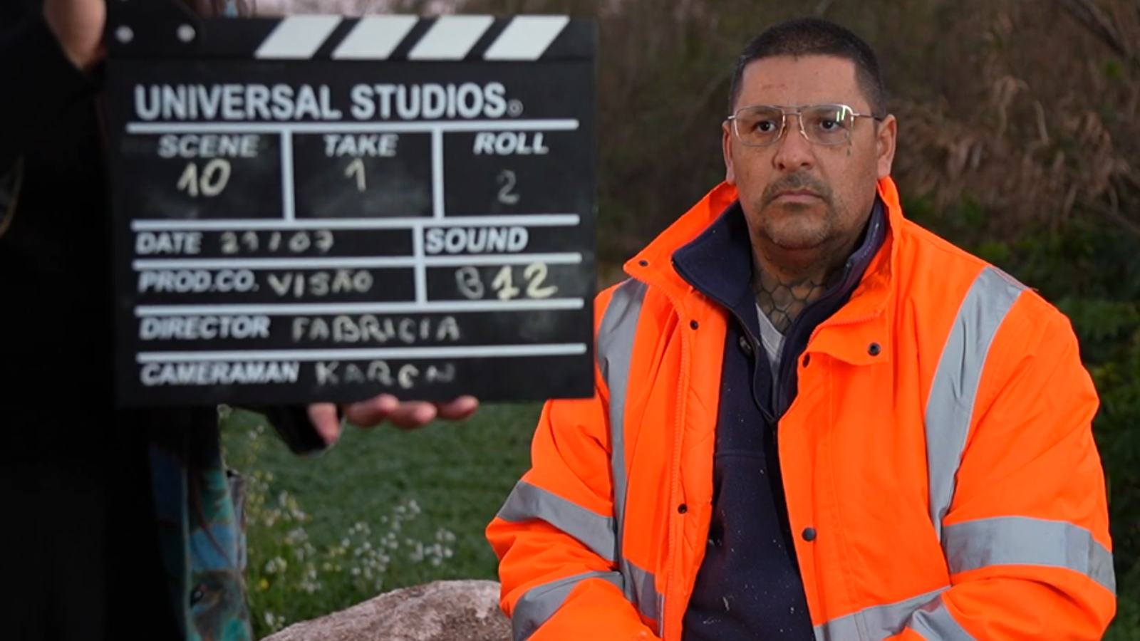 Interviewee in a high-visibility jacket beside a film clapperboard